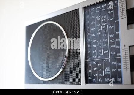 Detail view of a classic silver portable radio featuring a front speaker grille alongside an analog radio frequency display scale in soft indoor light Stock Photo
