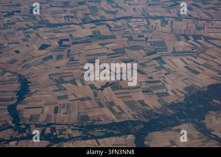 High altitude aerial view captured from an airplane window looking down at a large expanse of geometric agricultural crop fields forming a colorful mo Stock Photo