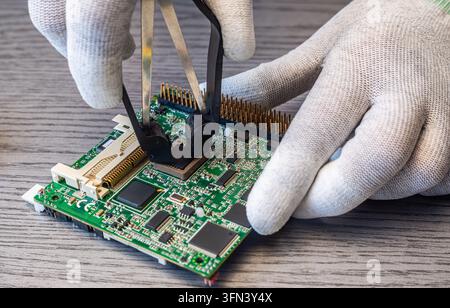 Technicians perform quality control by replacing components on a circuit board in a manufacturing environment during normal working hours. Stock Photo