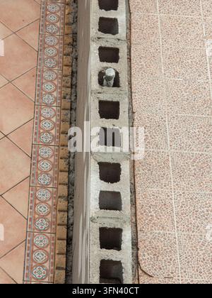 Construction workers are building a cinder block wall to separate two tiled patio floors. The wall is being placed where two different tile styles mee Stock Photo