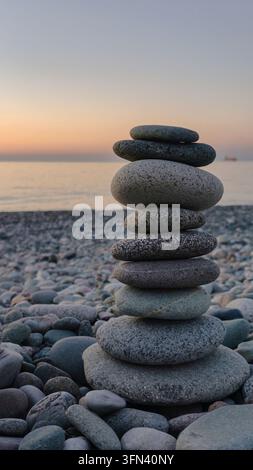 A balanced stack of smooth stones stands on a rocky seashore at sunrise or sunset, illustrating meditation, mindfulness, balance and peaceful connecti Stock Photo