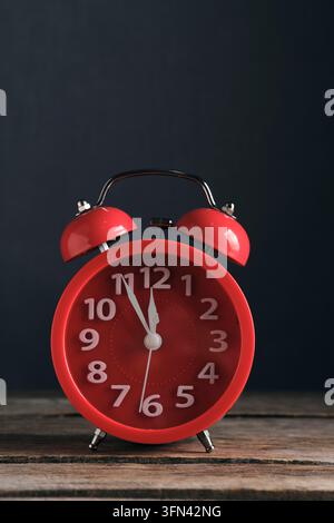 Bright red alarm clock standing on dark wooden surface against dark background, closeup view Stock Photo
