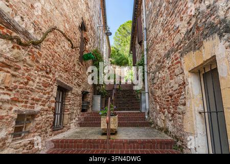 Scenic alleyway with stairs between ancient brick and stone houses in quaint historic medieval village Penne d'Agenais, Lot-et-Garonne, France Stock Photo