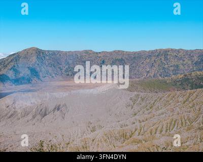 Volcanic Bromo crater dominates the rugged landscape. Sky above is clear, unblemished, deep blue Stock Photo