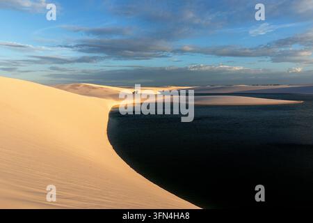 A rugged 4x4 vehicle parked on a white sand dune in Lencois Maranhenses, surrounded by turquoise lagoons under a magical golden sunset. Stock Photo