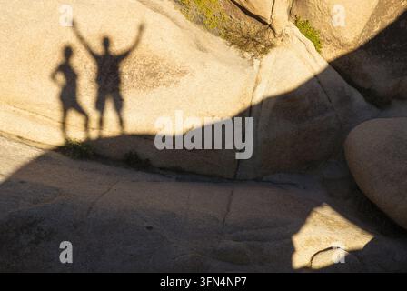View of the shadows of two people cast on a large textured rock formation in Joshua Tree, California, United States. Stock Photo