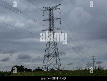 View of high-voltage electricity transmission pylons standing in a rural field under a cloudy sky in Jos, Plateau, Nigeria. Stock Photo
