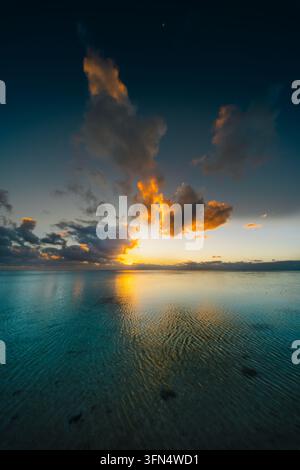View of the sunset over the calm turquoise waters of the Aitutaki lagoon with golden clouds reflecting on the surface in the Cook Islands. Stock Photo