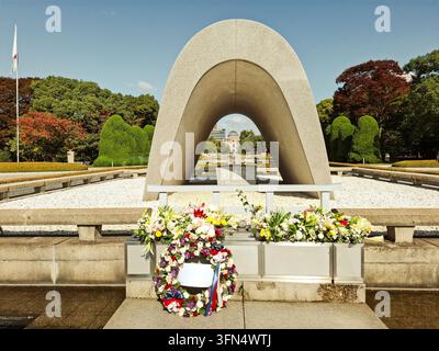 View of the Hiroshima Peace Memorial Cenotaph with floral wreaths and colorful flowers in the Hiroshima Peace Memorial Park in Hiroshima, Hiroshima, J Stock Photo