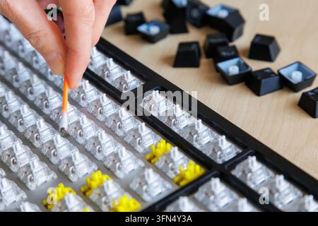 Close-up hand removing visible dust, dirt from disassembled computer keyboard, detailed cleaning between switches, computer hygiene, preventive mainte Stock Photo