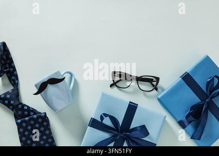 Blue wrapped gifts, necktie, eyeglasses and a cup decorated with a mustache arranged on a light blue background. Father's Day gift and celebration con Stock Photo