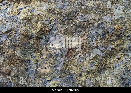 Rough natural rock texture with weathered grey and golden mineral surface, abstract geological pattern background of raw stone structure detail Stock Photo