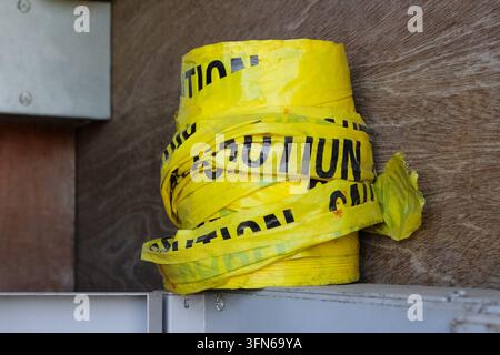 A roll of yellow caution tape sits bunched up on a metallic structure against a weathered wood background. Stock Photo