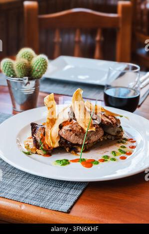 A tuna steak topped with crisp yuca chips and finished with mojo sauces waits on a restaurant table. Canarian speciality cooking for food tourism and Stock Photo