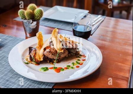 A plated tuna steak with mojo sauces and yuca chips sits on a wooden table in a Canarian restaurant. Island gastronomy for travel dining and hospitali Stock Photo