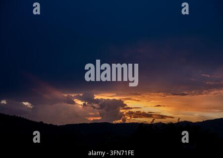 Dramatic sunset over mountain silhouettes with a gradient sky from deep blue to bright orange and gold, soft clouds glowing at golden hour, peaceful s Stock Photo