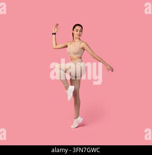 Balance And Endurance. Studio shot of beautiful young sportswoman standing on one leg, doing exercise, standing in high knee pose isolated over pink b Stock Photo