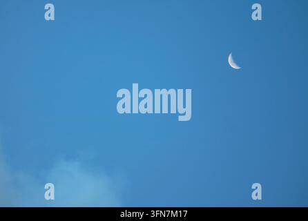 Sharp daytime moon with visible surface craters against a clear blue sky background Stock Photo