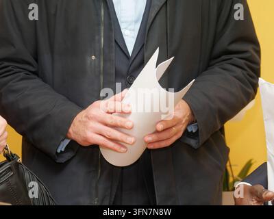 Close-up of a man in a suit and coat holding rolled white paper indoors with a yellow wall background. Stock Photo