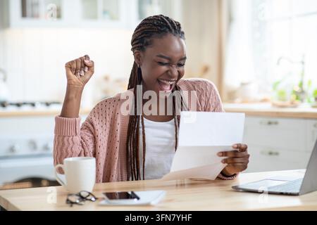 Good News. Portrait Of Overjoyed African American Lady Reading Letter In Kitchen, Euphoric Black Woman Raising Fist And Exclaiming With Excitement, Em Stock Photo