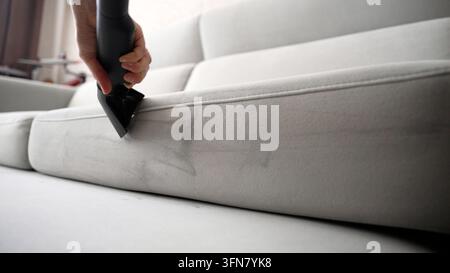 Professional cleaner hand uses extraction machine on dirty couch. Visible stripe shows clean fabric after removing dirt. Upholstery maintenance and de Stock Photo
