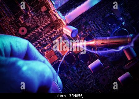 Close-up of a soldering iron repairing a computer motherboard, glowing tip melting solder on microchips and components under neon blue and purple ligh Stock Photo