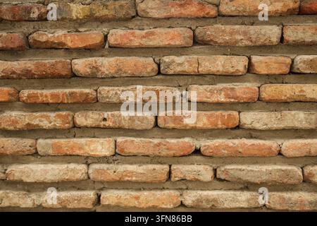 Weathered red and beige brick wall with irregular masonry, rough mortar joints, and aged textured surface as architectural background Stock Photo