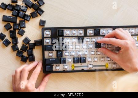 Hand reinstalling keycaps on cleaned computer keyboard, restoring removed keys after deep cleaning, DIY reassembly, computer hardware maintenance at h Stock Photo