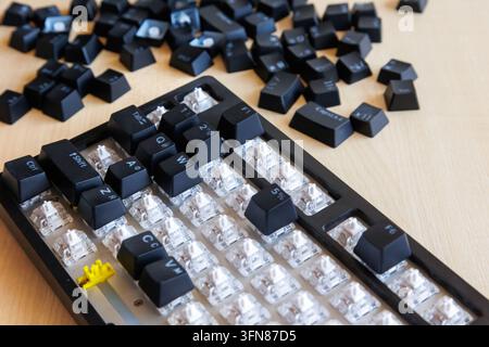Partially reassembled computer keyboard with removed keycaps scattered nearby, restoring keys after deep cleaning, DIY hardware maintenance, repair pr Stock Photo