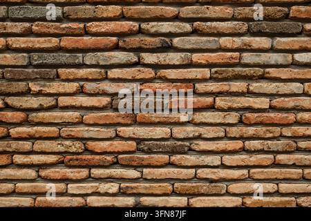 Weathered red and brown brick wall with irregular masonry, aged mortar, and textured horizontal pattern forming a rustic architectural background Stock Photo