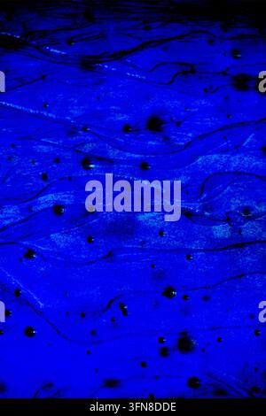 Deep cobalt blue liquid abstract texture with dark spots, evoking a sense of mysterious ocean depth or ink dispersing in water, perfect for fluid art Stock Photo