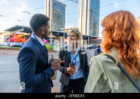 Diverse business professionals having an informal conversation and networking while holding coffee and reusable bottles in a modern city street enviro Stock Photo