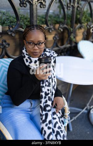 Stylish young woman with glasses enjoys coffee outside Stock Photo