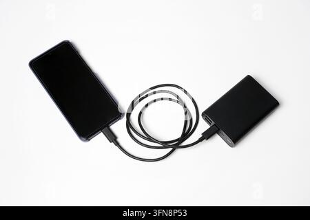 Smartphone connected to a portable power bank with a charging cable on a white background, illustrating mobile charging and backup energy Stock Photo