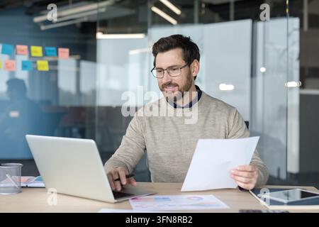 Professional businessman analyzing data and checking business documents while typing on a laptop, demonstrating concepts of busy work, finance, and productivity in a modern office Stock Photo