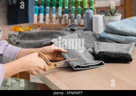 Sustainable fashion and clothing repair, person cutting denim jeans with scissors for upcycling and tailoring in a sewing workshop Stock Photo