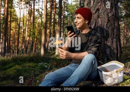 Man using smartphone app for mushroom identification in autumn forest. Scanning wild edible fungi with a smartphone camera checks safety, bolete speci Stock Photo