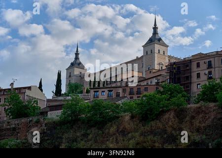 The Alcázar of Toledo towering over old houses and the green slopes above the River Tagus under a cloudy sky, Spain Stock Photo