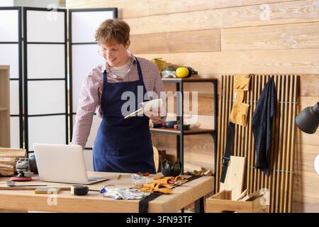 Small business management and digital transformation, carpenter using laptop for project planning and inventory in a modern woodworking workshop Stock Photo
