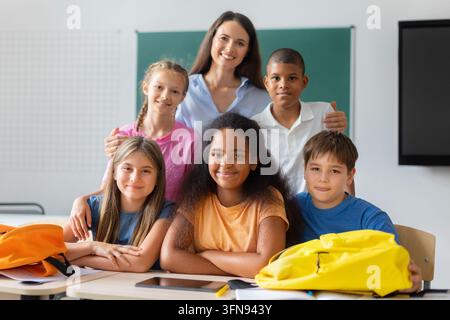 Female teacher posing with diverse group of elementary school students in classroom Stock Photo