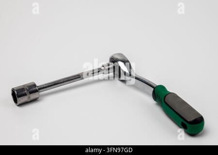 Chrome ratchet wrench with green and black handle rests on clean white surface. Long extension bar connects to hexagonal socket. Metal parts show knur Stock Photo