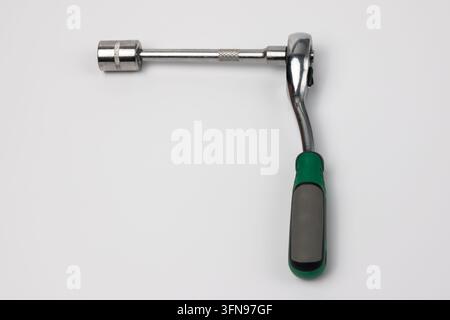 Chrome ratchet wrench with green and black handle rests on clean white surface. Long extension bar connects to hexagonal socket. Metal parts show knur Stock Photo
