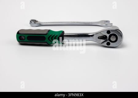 Chrome ratchet wrench with ergonomic green and black handle positioned beside double ended wrench on clean white background. Metal hand tools featurin Stock Photo