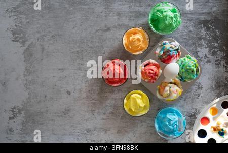 Creative Easter composition featuring colorful marbled eggs resting in small glass bowls with watercolor paints and brushes on a gray background with Stock Photo
