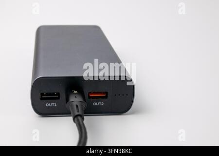 Grey portable power bank connected to USB cable on white background. Rechargeable external battery pack for mobile devices and electronic gadgets. Mod Stock Photo