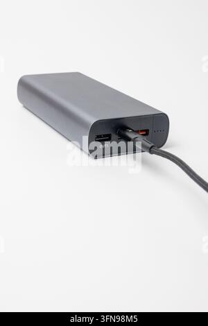 Grey portable power bank connected to USB cable on white background. Rechargeable external battery pack for mobile devices and electronic gadgets. Mod Stock Photo