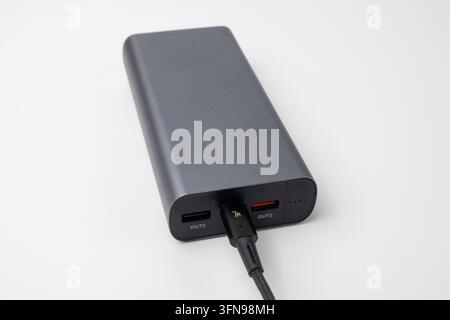 Grey portable power bank connected to USB cable on white background. Rechargeable external battery pack for mobile devices and electronic gadgets. Mod Stock Photo
