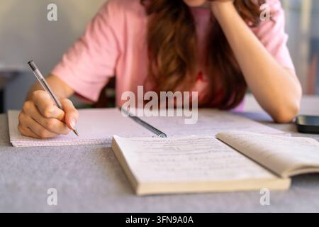 Close-up of a student hand writing with a ballpoint pen in a spiral grid notebook next to an open math textbook, teenager face out of frame. Concept o Stock Photo