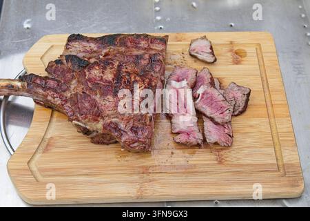 A freshly grilled medium-rare tomahawk ribeye steak sliced into thick, juicy pieces on a wooden bamboo cutting board. Stock Photo