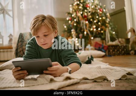 Boy Using Digital Tablet on Floor near Christmas Tree at Home Stock Photo